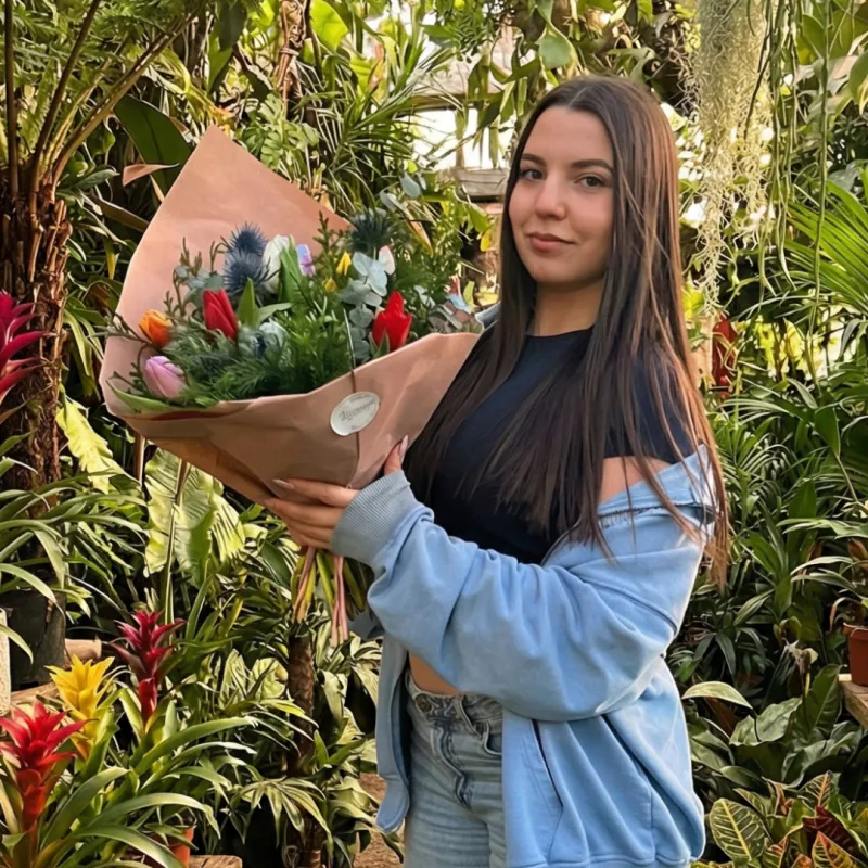 Alumna con su ramo envuelto en papel kraft entre plantas tropicales